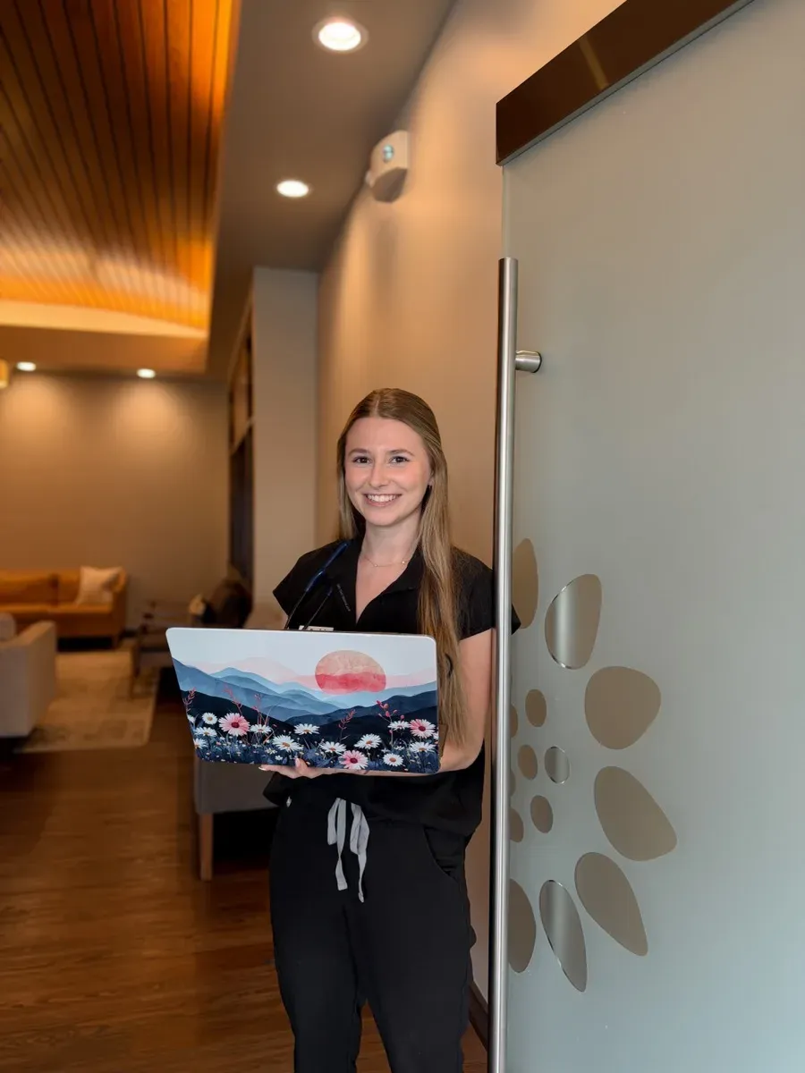 A Prairie Health & Wellness team member smiling in the clinic hallway, holding a laptop